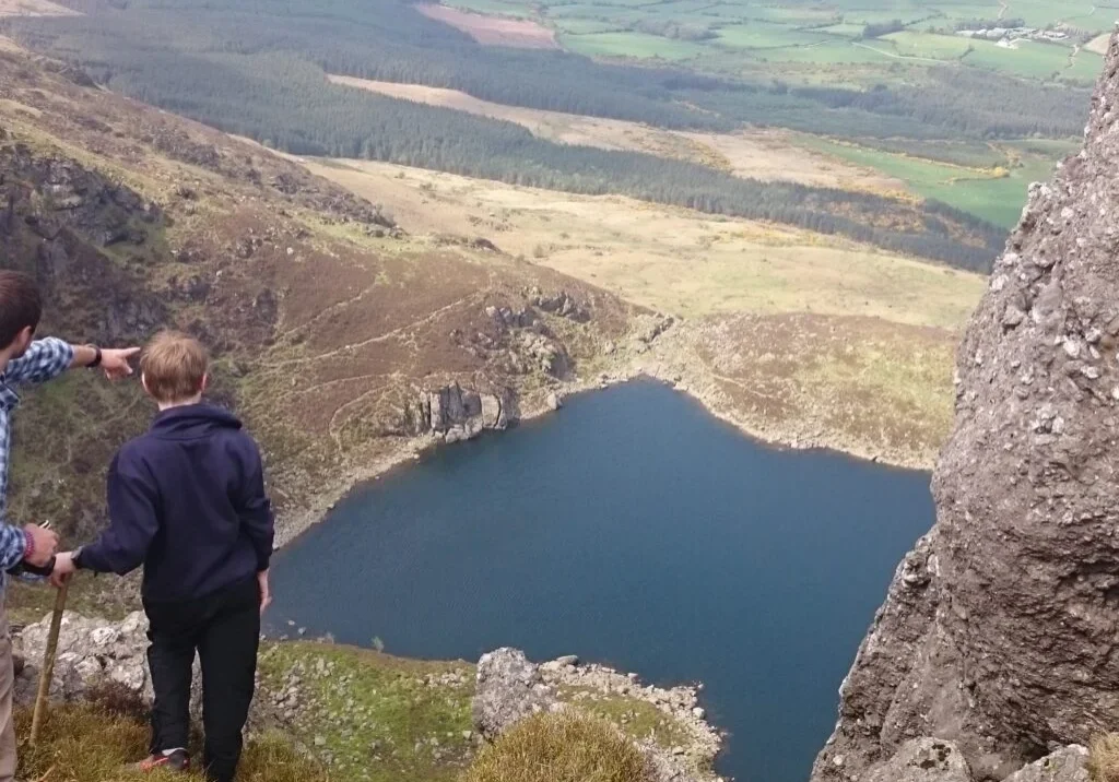 Man showing a boy a lake from atop of mountain.
